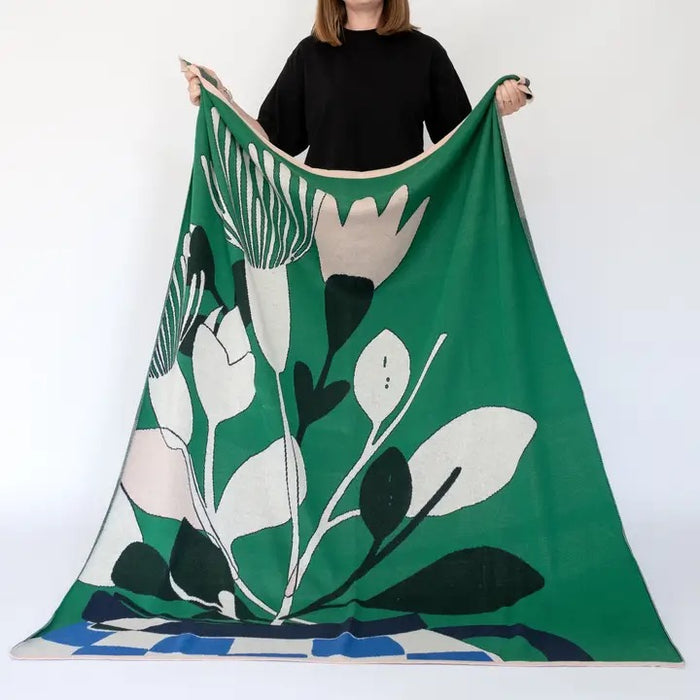 Person holding an Ivory, blush pink floral design throw with a blue checkered vase on a green background