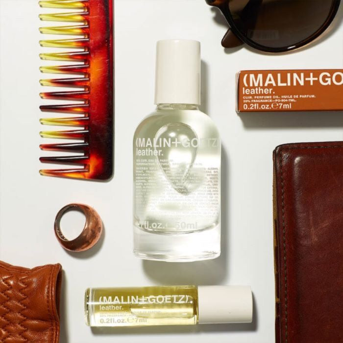 MALIN+GOETZ leather eau de parfum with other products including a bottle, roller ball, and comb on a white surface.