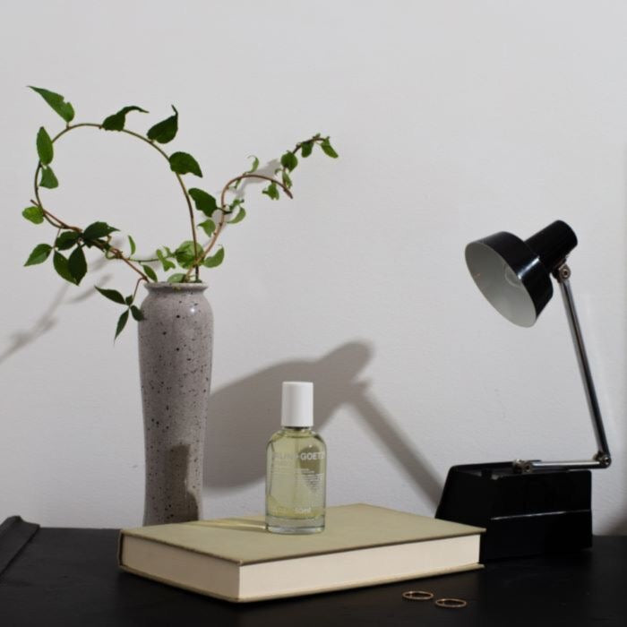 Malin+Goetz cannabis eau de parfum on a desk setup with a vase, book, and lamp against a plain background