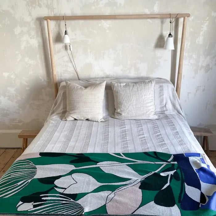 Bed with a wooden headboard and floral blanket in a room with light-colored walls.