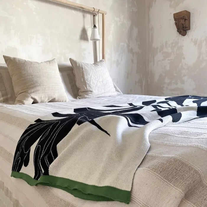 Bed with a decorative throw featuring black and ivory leaf patterns in a bedroom setting.