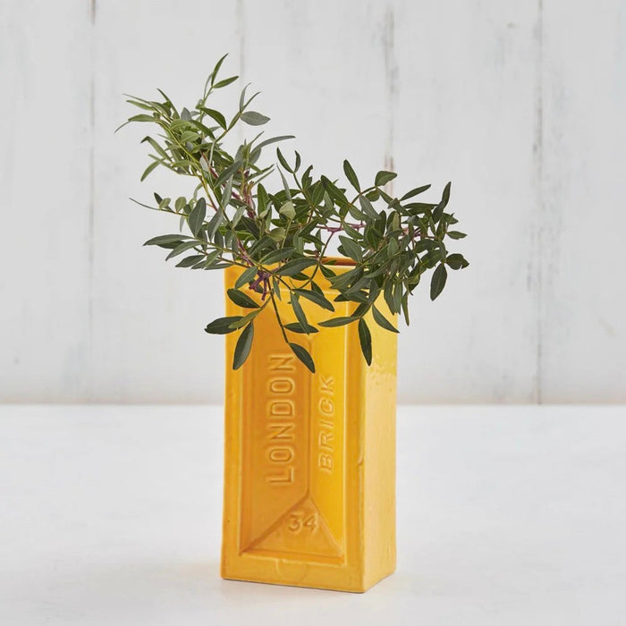 Yellow London brick-shaped vase with green plant against a white background