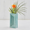 Turquoise London brick-shaped vase with an orange tulip and green leaves on a white background