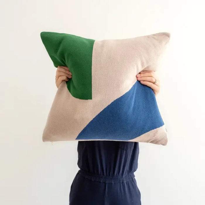 Person holding a geometric cushion with green, pink, and blue sections on a white background