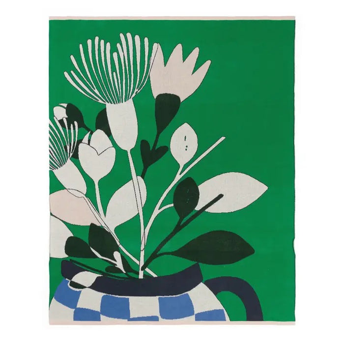 Ivory, blush pink floral design throw with a blue checkered vase on a green background