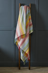 Rainbow striped woollen throw draped over a wooden ladder against a dark gray wall.