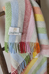 Woollen rainbow striped throw with a brand label on a wooden surface
