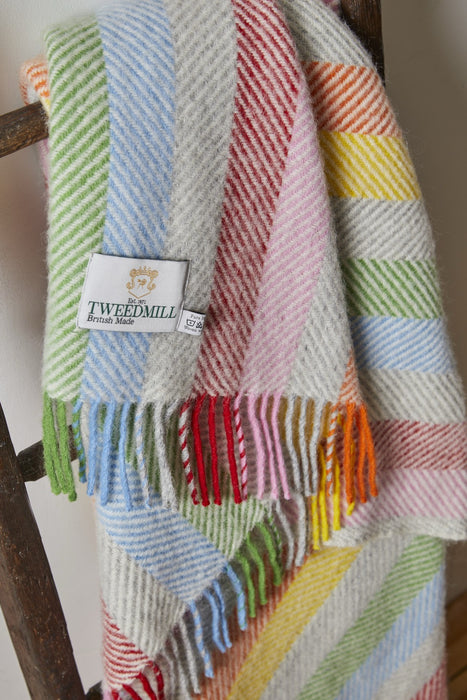 Woollen rainbow striped throw with a brand label on a wooden surface