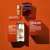 MALIN+GOETZ leather eau de parfum with other products including a bottle, roller ball, and candle on a tan surface.