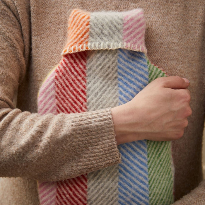 Person holding a colourful striped woolen hot water bottle and cover against themselves