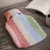 Colorful striped hot water bottle and cover cover on a wooden surface with an open book and cup of coffee.