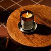 Amber glass candle jar labeled 'Smoke & Musk' by 'Earl of East', hand poured in London on a dark green background. the candle is lit and placed on a small wooden table.