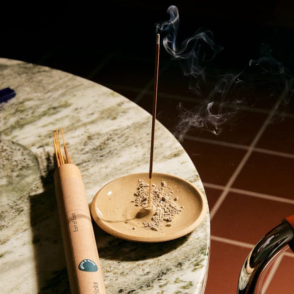 Incense stick burning in a holder with a lit incense stick on a stone surface.