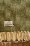 Close-up of a green Tweedmill woollen throw with a fishbone pattern and brand label.