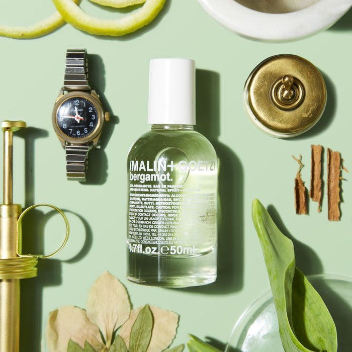 Bottle of Malin+Goetz bergamot eau de parfum on a green surface with decorative items.