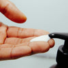 Hand applying white cream from a black pump dispenser.