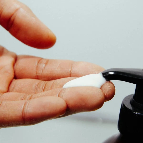 Hand applying white cream from a black pump dispenser.