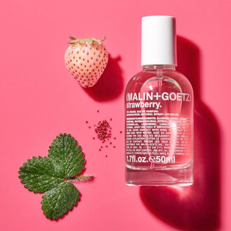 Malin+Goetz Strawberry perfume bottle with a strawberry and leaf on a pink background