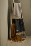 Three fishbone pattern throws in various colours draped over a wooden ladder against a beige wall.