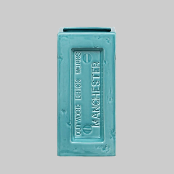 Turquoise brick-shaped vase with 'Outwood Brick Works Manchester' text on a gray background.Perfect for design lovers who appreciate function with an industrial edge.