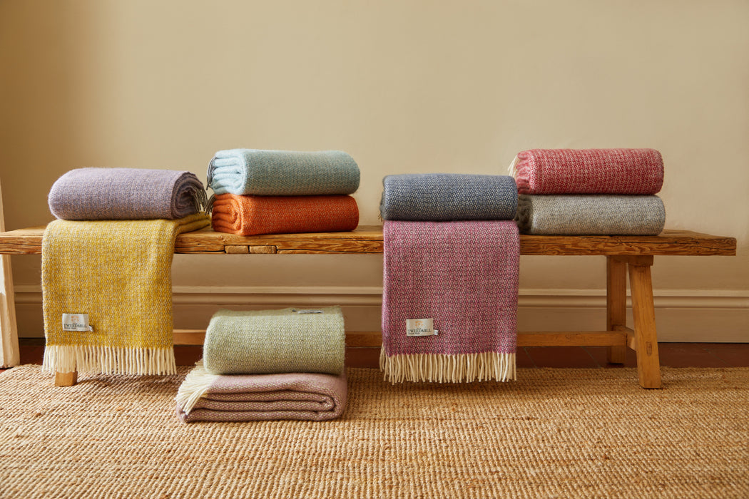 Stacks of colorful illusion patterned blankets on a wooden bench against a beige wall.