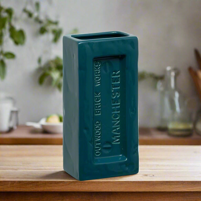 Teal ceramic vase with 'Manchester' text on a wooden surface.Perfect for design lovers who appreciate function with an industrial edge.