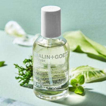 Malin+Goetz bottle on a light green background with leaves and flowers.