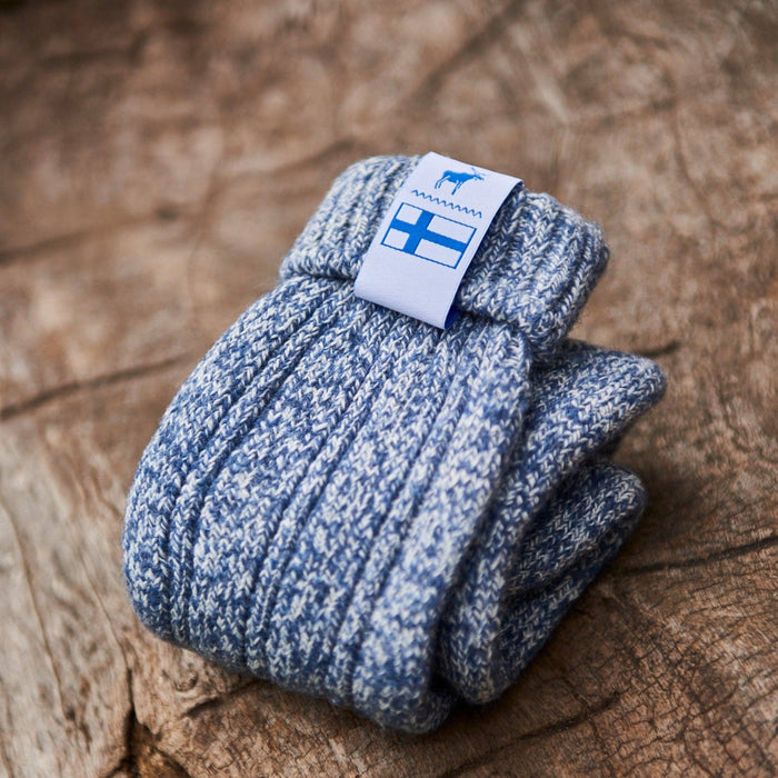 Folded baltic blue knitted Sisu of Finland socks with a Finnish flag brand label on a wooden log background. Lambswool and cotton rich to get you through the cold Arctic nights.