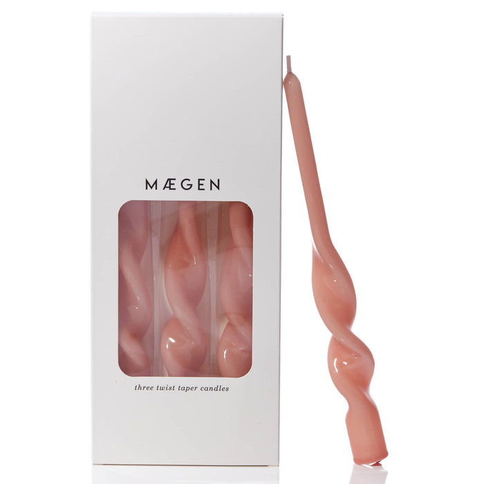 Plaster pink twisted taper candle leaning against branded Máegen white box packaging with see through window on a white background