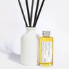 Elegant, white ceramic and reusable diffuser with black reeds and a glass bottle with aluminium screw top lid filled with fragrance oil on a light background