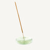 Incense stick in a round handblown transparent pale green glass holder on a white background