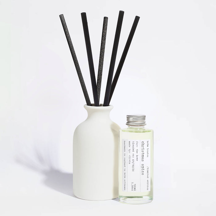 Elegant, white ceramic and reusable diffuser with black reeds and a glass bottle with aluminium screw top lid on a light background